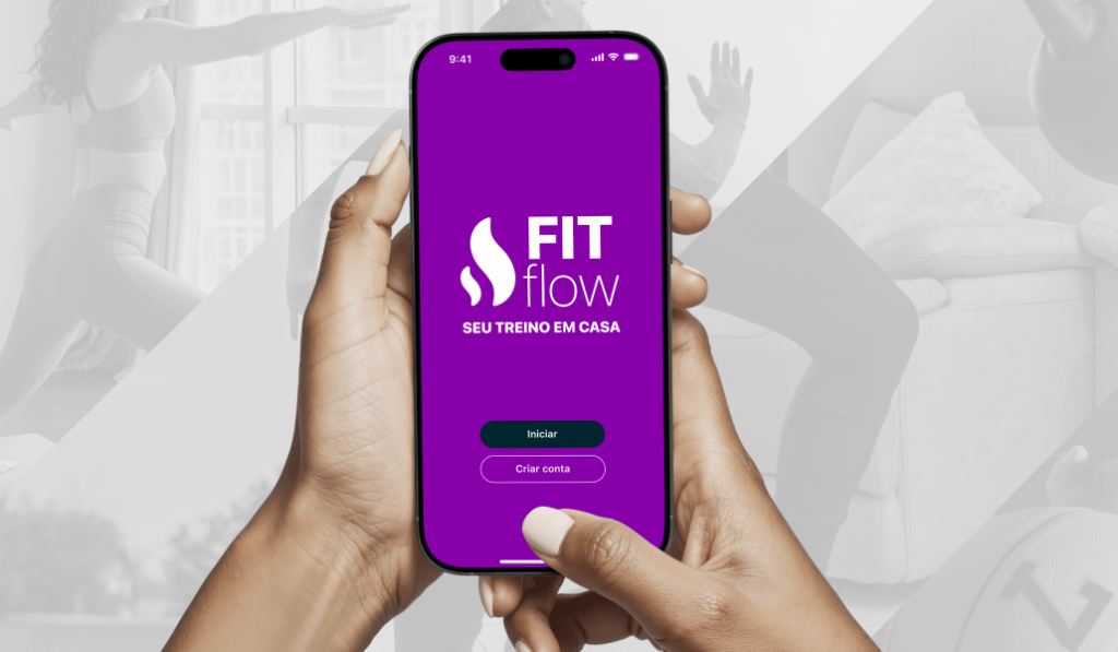 Smartphone segurado por duas mãos exibindo a tela inicial do aplicativo de fitness FIT Flow com fundo roxo, logotipo do app, texto “Seu treino em casa” e botões “Iniciar” e “Criar conta”. Ao fundo aparecem imagens desfocadas de pessoas praticando exercícios.